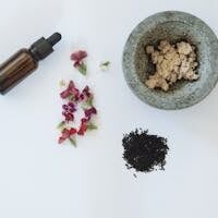 Flat lay of natural skincare ingredients including flowers, black seeds, and a dropper bottle.